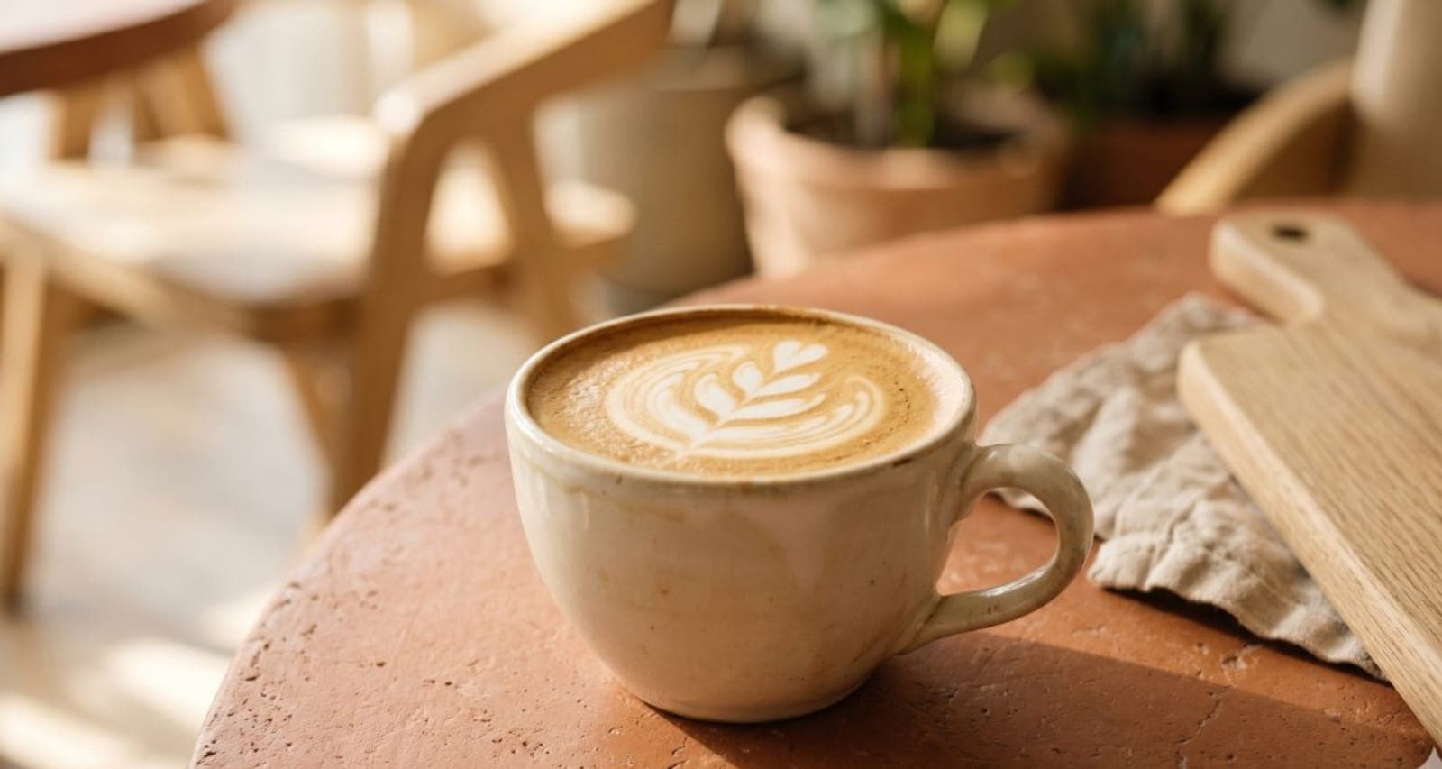 A cappuccino with latte art on a warm terracotta café table — appetite-setting visual, not a specific offer.