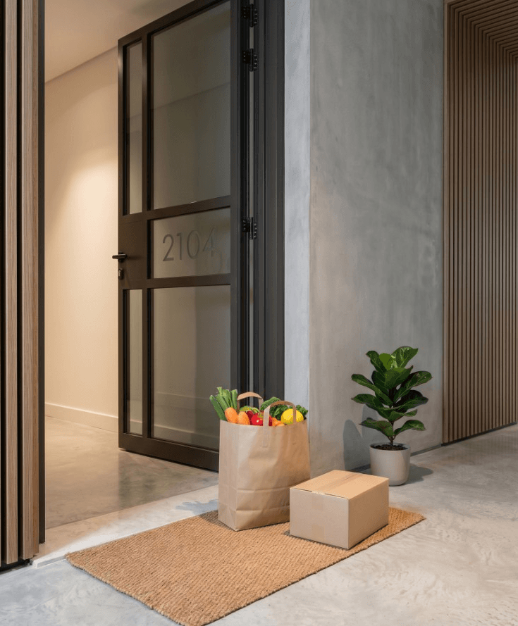 Grocery delivery and a cardboard package left on a doormat outside a modern apartment door numbered 2104 in Dubai Creek Harbour.